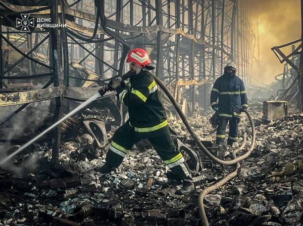 Рятувальники ліквідовують пожежу, що виникла внаслідок російської атаки БпЛА на Київщину 12 серпня. Судячи з вигорілих стелажів на фото, йдеться про великий маркет або логістичний центр